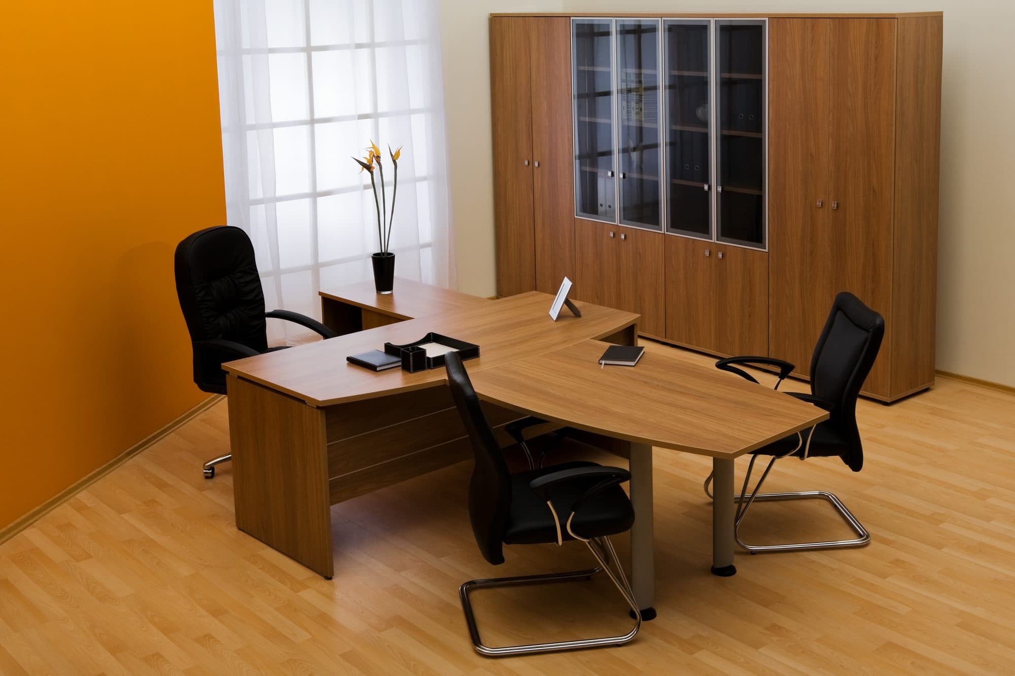 Sala de escritório com mesa em L, cadeira presidente, cadeiras de espera e armário com portas em vidro